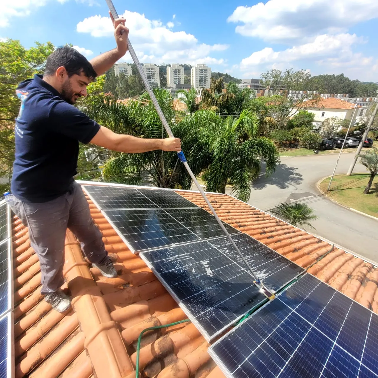 Profissional da Alpha Services limpando placas solares sobre o telhado de uma casa.